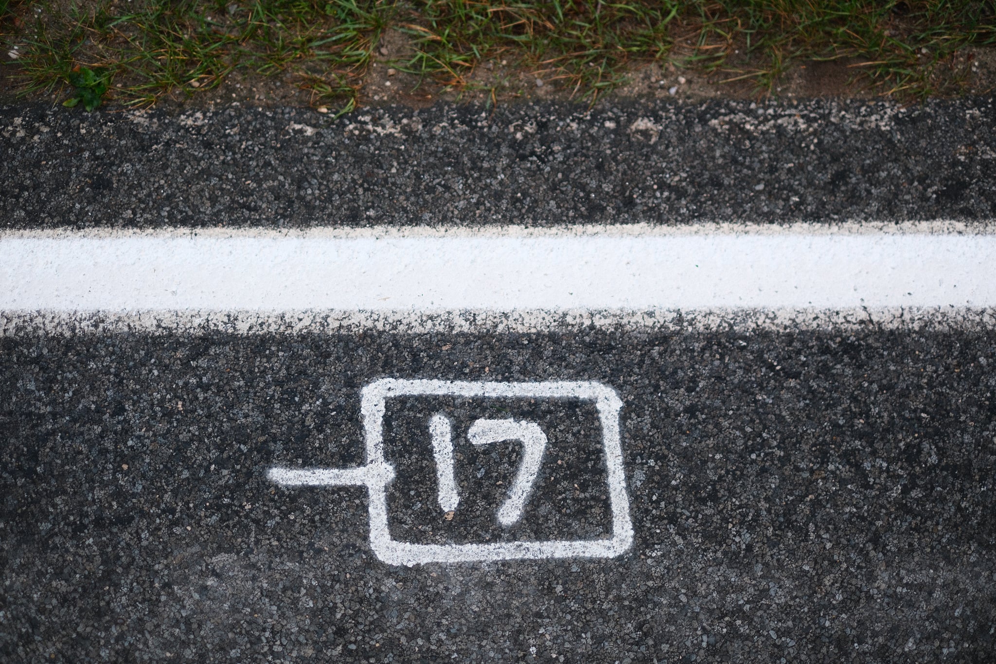 White stencil of a plug-like icon with the number 17 on a dark asphalt road beside a solid white line