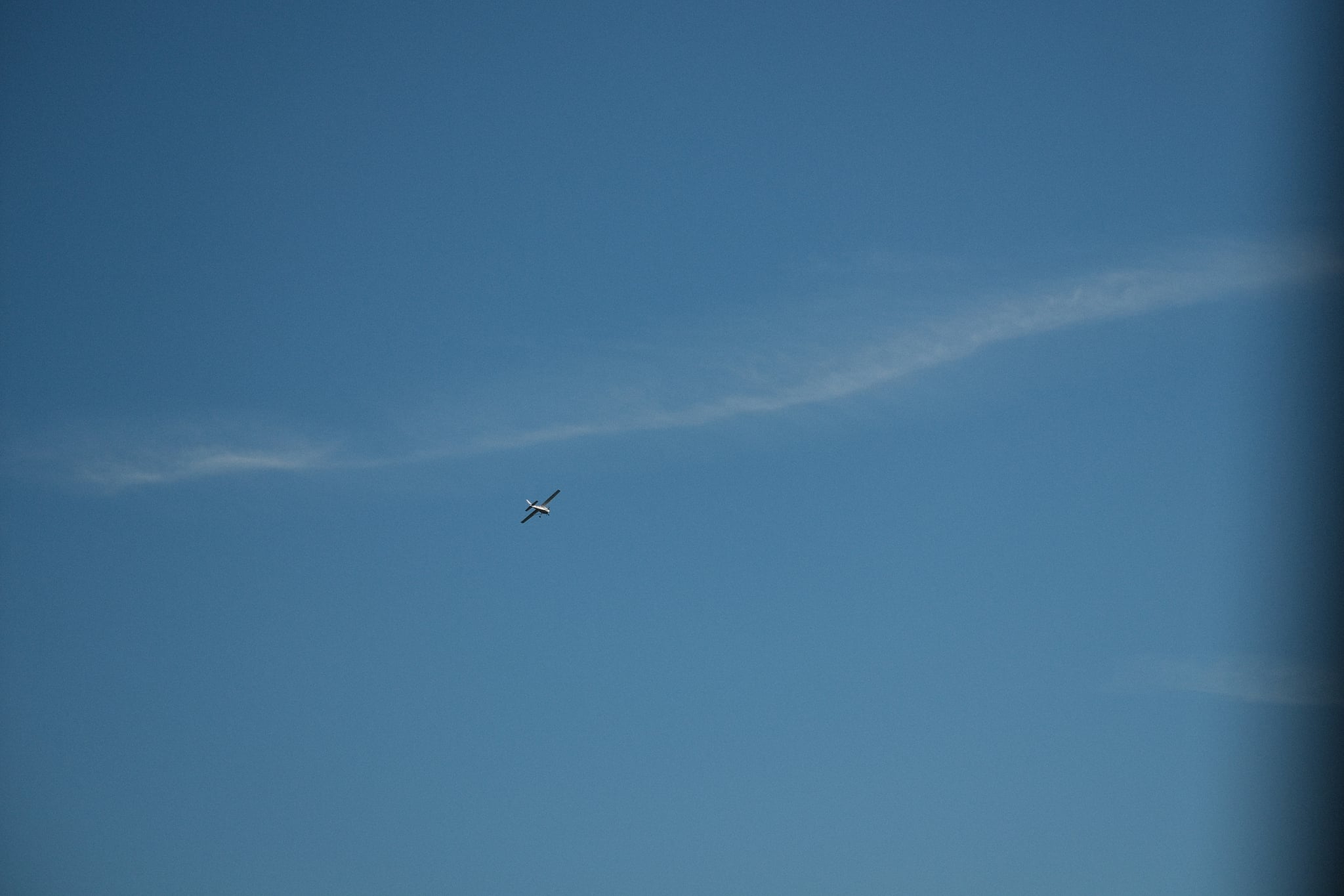 A vast blue sky with a long, thin cloud and a small airplane flying nearby