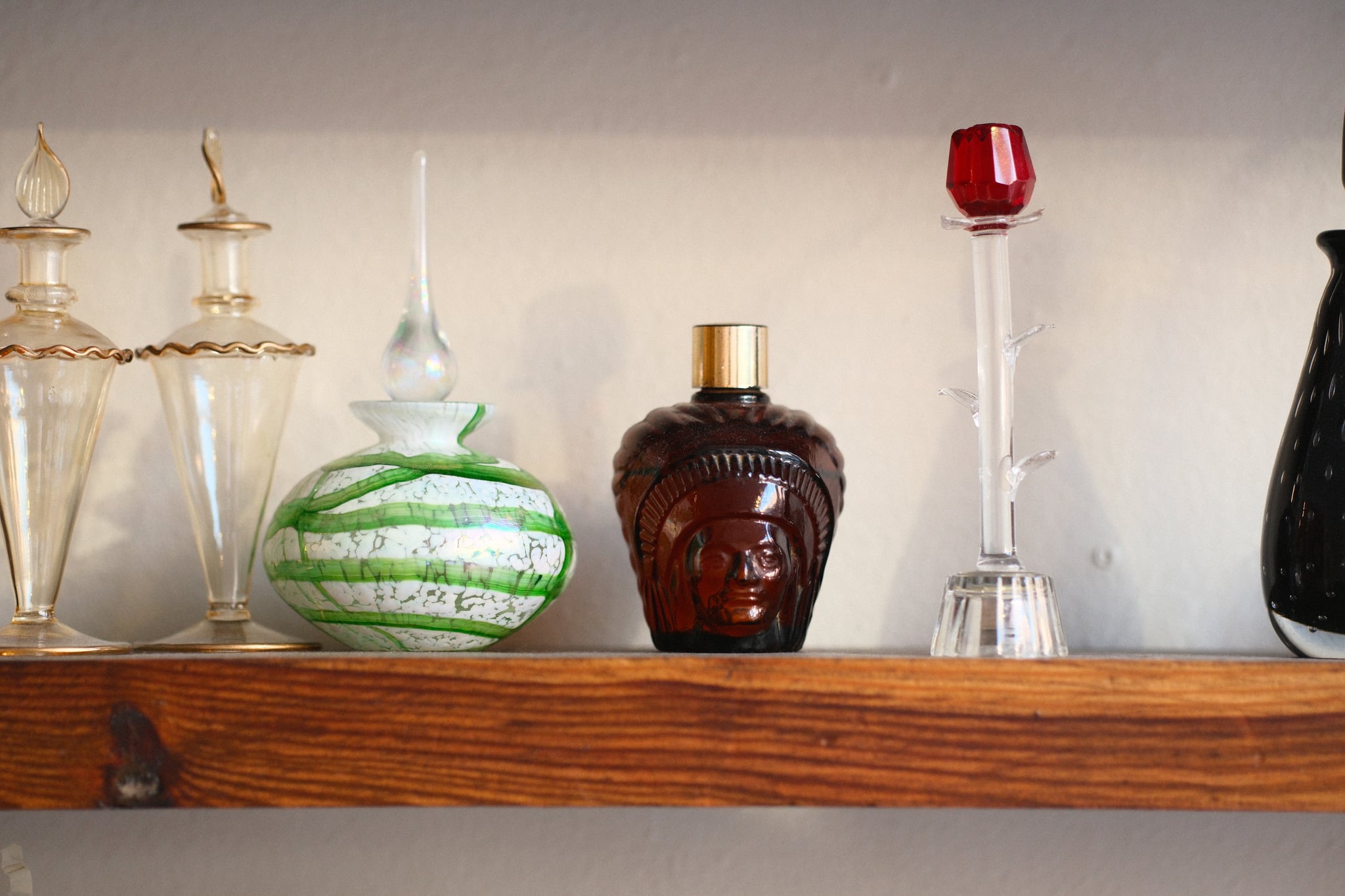 Row of decorative glass bottles and a green-striped vase on a wooden shelf against a light wall
