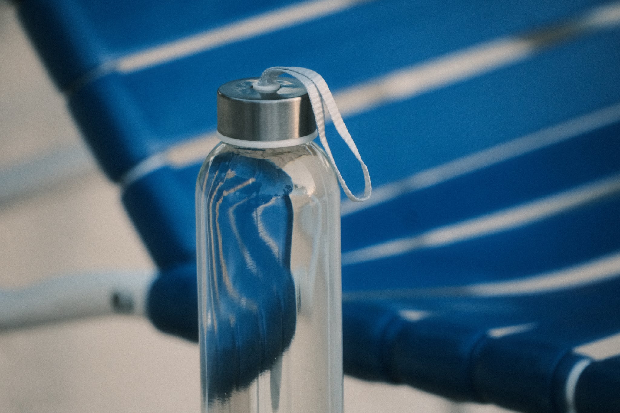 Reusable metal water bottle on a blue-striped beach chair in sunlight
