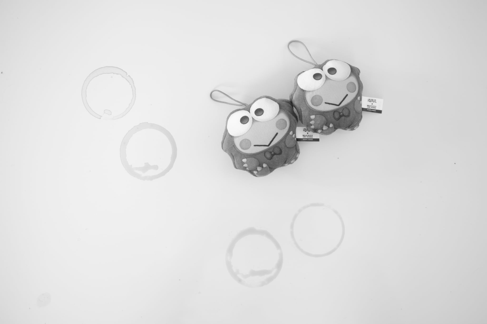 Two cartoon frog keychains with large eyes are placed on a light surface, surrounded by several faint circular marks