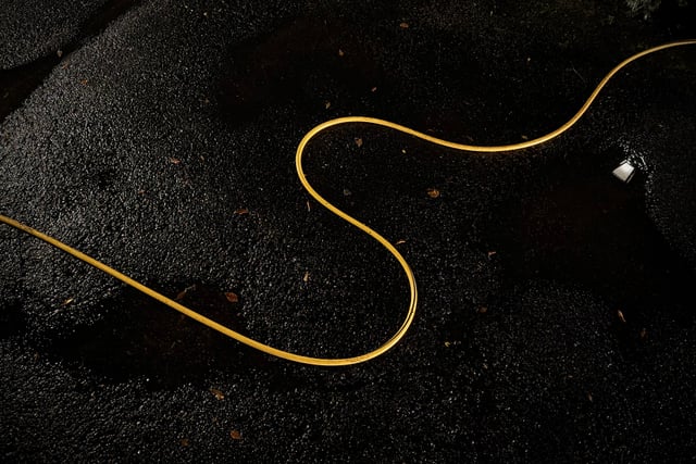 A thin yellow cord winds in graceful curves across a dark, grainy surface
