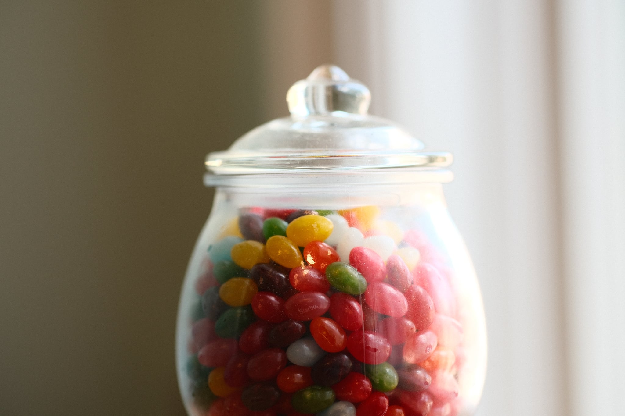 A glass jar filled with colorful jelly beans, topped with a clear lid, against a softly lit background