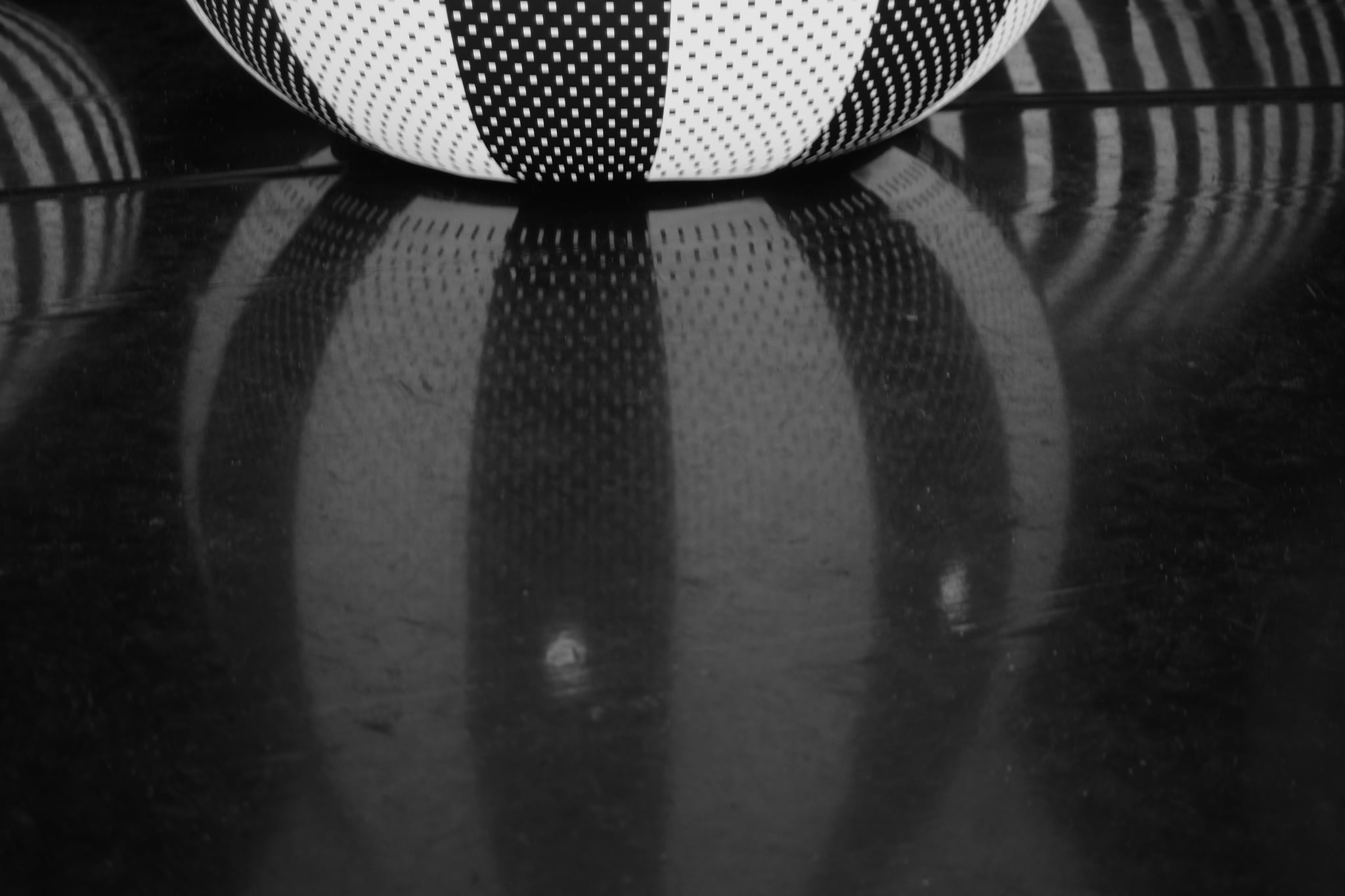 Close-up of a black-and-white checkered object resting on a glossy dark surface with a soft reflection