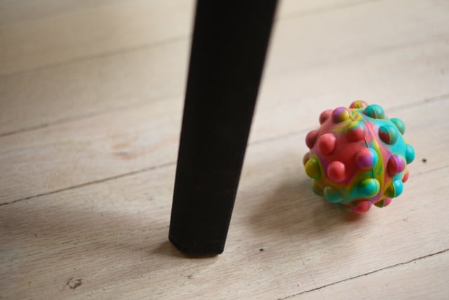 A colorful, textured ball on a wooden floor next to a black table leg