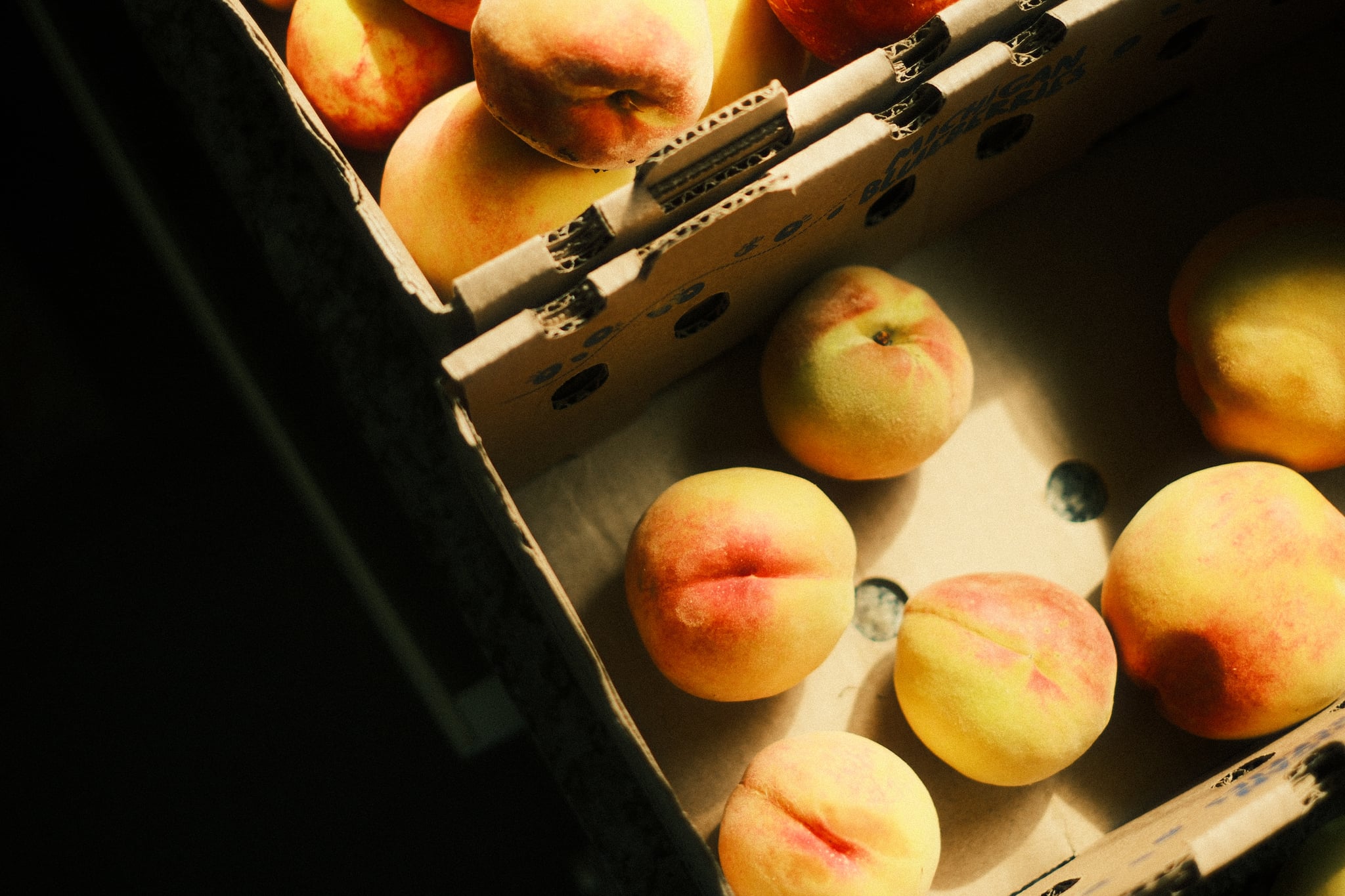 Ripe peaches in a wooden crate under warm light