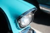 A close-up of a turquoise vintage car's headlight with chrome trim