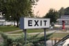 Large roadside EXIT sign on metal posts near a parking area and trees at dusk