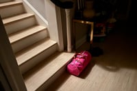 A pink duffle bag rests at the foot of a staircase bathing in a beam of light, with the surrounding area in soft shadows