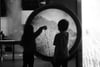 Two children are silhouetted against a large circular interactive display, with one child reaching out to touch it The scene is in black and white, creating a dramatic contrast