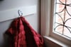 A red puffer jacket hanging on a white hook next to a window with decorative ironwork
