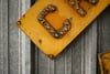 Yellow riveted metal plate with a raised letter C lying diagonally on weathered gray wooden planks