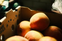 Ripe peaches piled in a cardboard produce crate under warm light
