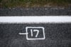 White stencil of a plug-like icon with the number 17 on a dark asphalt road beside a solid white line