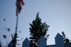 A white picket fence with a tree and an American flag in the background, set against a clear sky