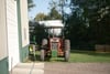 A red tractor parked on grass near a building, with trees and hay bales in the background