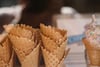 Stack of waffle cones in the foreground with a sprinkled ice cream cone in the background