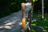 A wooden post with an orange marker stands beside a narrow, winding road surrounded by greenery and trees