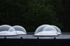 Row of translucent dome skylights on a flat rooftop against a dark treeline backdrop